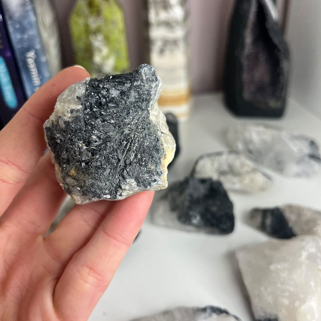 A close-up view of a hand holding a highly textured raw quartz crystal piece with a solid cap of black tourmaline mineral matrix, illustrating a grounding pocket talisman that helps dissolve chaotic mental clutter.