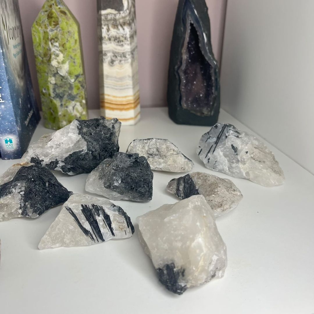 A cluster layout of various raw tourmaline in quartz crystal specimens displayed on a white shelf, showcasing stark black needles embedded within frosty quartz points to create a powerful energetic shield for your home entryway.
