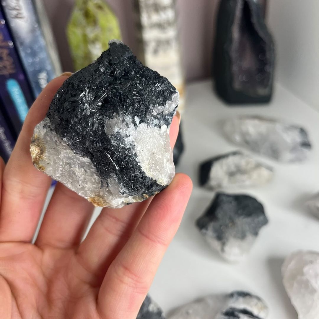 An open palm supporting a compact raw tourmaline in quartz specimen, highlighting the cold, rugged contours and striking dark line features to anchor a quiet moment of focus and personal grounding rituals.