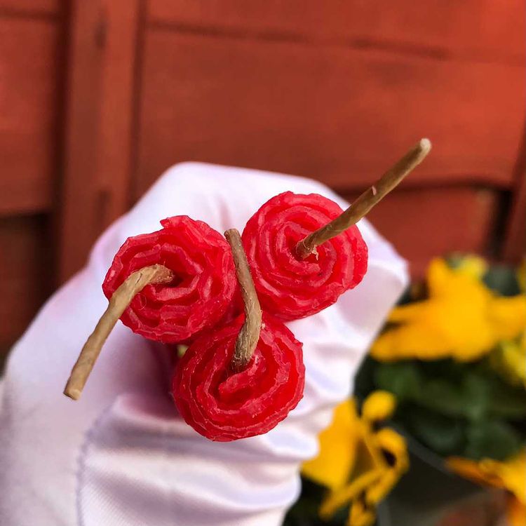 A top-down macro shot looking straight onto three red beeswax manifestation candles bundled tightly in a white gloved hand. The unique perspective captures the crisp, concentric circular layers of the hand-rolled honeycomb design surrounding the unlit natural linen wicks.