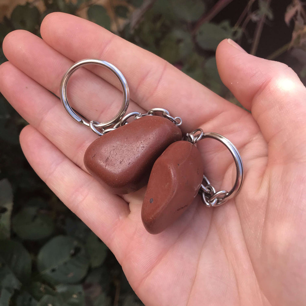 Two Red Jasper keychains held outdoors in natural daylight, showcasing crimson hues and organic patterns as a daily travel anchor.