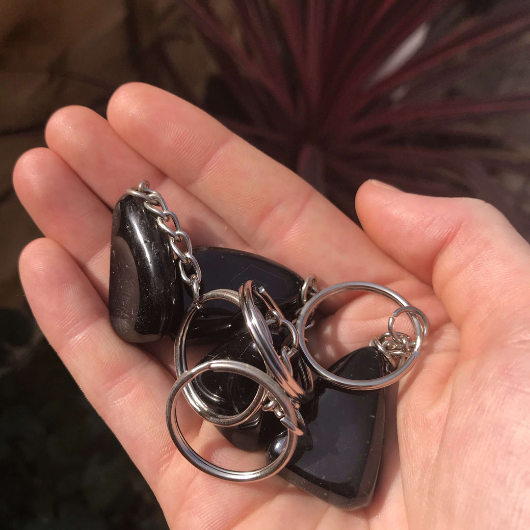 A person holding a group of polished black onyx crystal charms on silver metal keyrings, catching soft outdoor light.