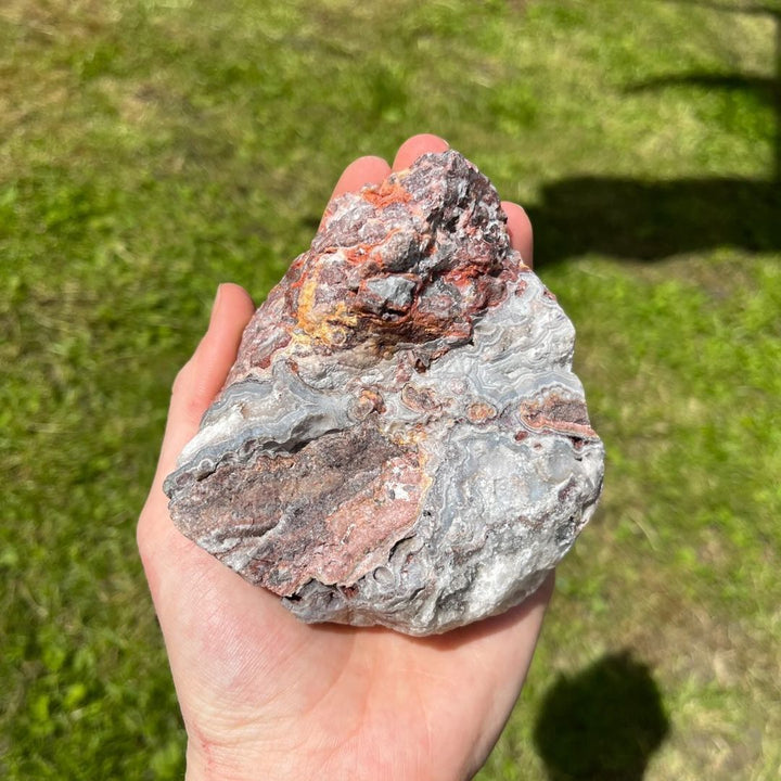 A hand holding a large rough crazy lace agate stone, detailing the complex winding patterns and natural earthy fracture lines that display the craftsmanship of nature and bring a cheerful frequency to your daily environment.