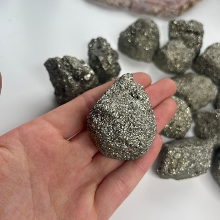 A person cradling a cluster of rugged, metallic raw pyrite stones in their palm to showcase their natural geometric fractures.