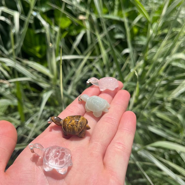 A hand presenting a group of tiny pocket-sized crystal animals, featuring a detailed brown Tiger Eye turtle carving.