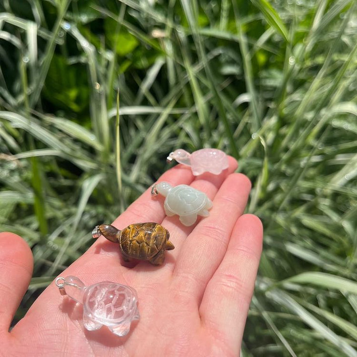 A hand presenting a group of tiny pocket-sized crystal animals, featuring a detailed brown Tiger Eye turtle carving.