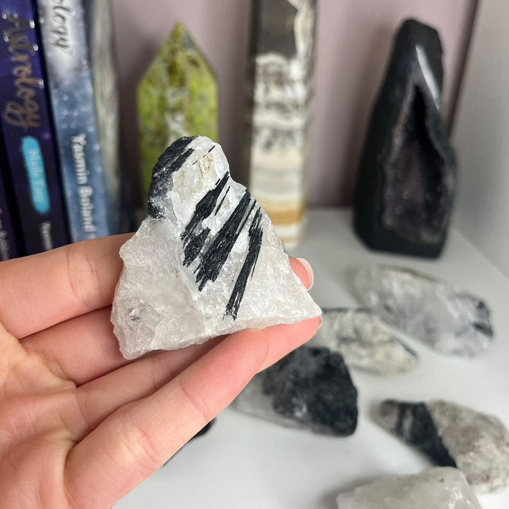 A hand presenting an unpolished piece of tourmalinated quartz crystal, highlighting distinct geometric black inclusions cutting sharply through a crisp white matrix to act as a fierce energetic shield against outside stress.