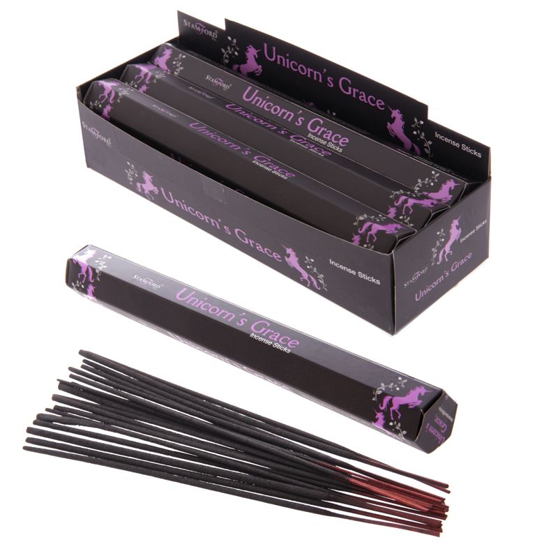 A studio product shot of a black and purple cardboard wholesale counter display box filled with packs of Stamford Unicorns Grace incense sticks against a clean white background. A single hexagonal individual 15g pack and a loose bundle of brown hand-rolled incense sticks rest neatly in the foreground, showcasing the mystical unicorn branding designed to bring a sweet aloe vera aroma and a soft calm to your favourite room.