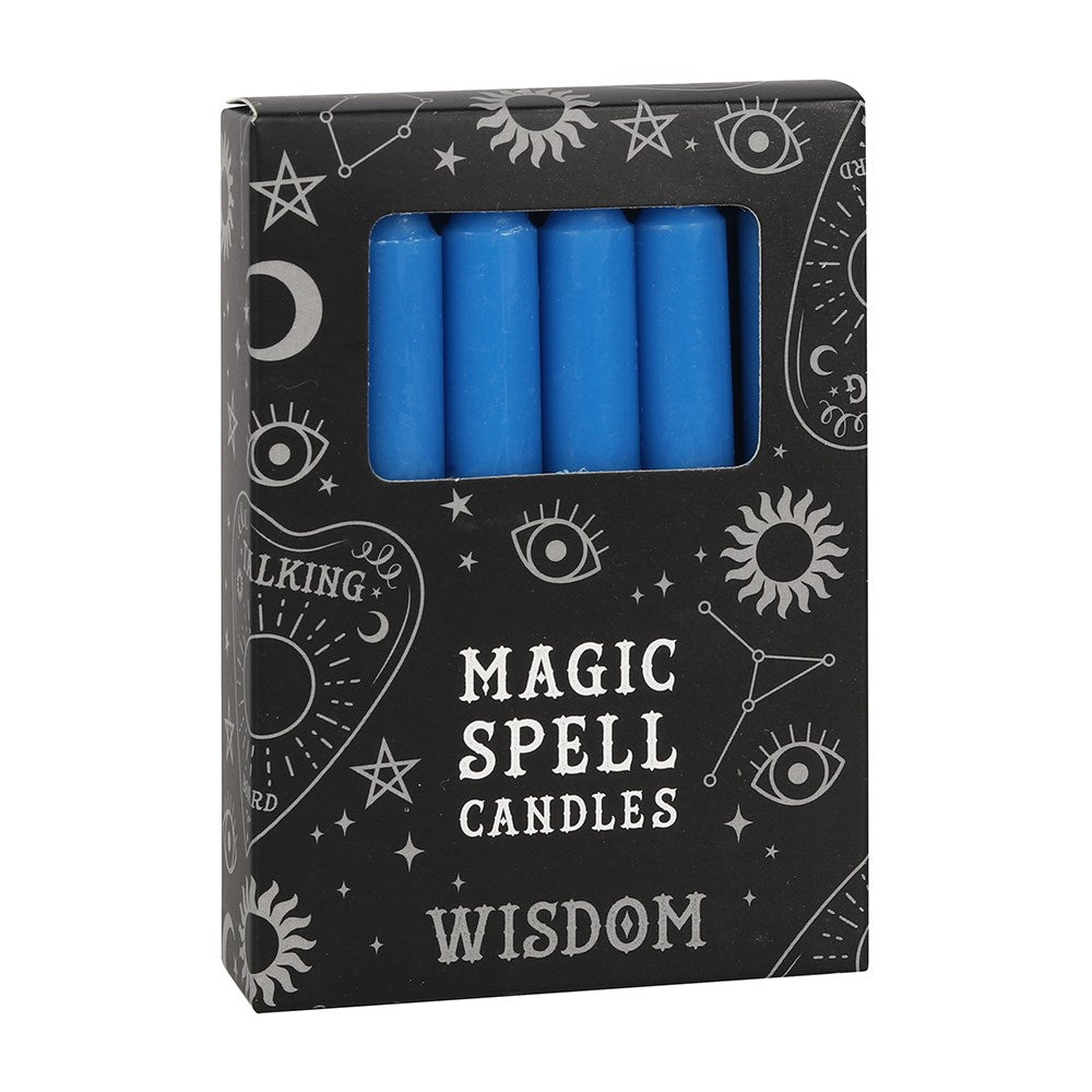 A three-quarter view of a black cardboard pack of Wisdom spell candles against a white background. The box displays mystical white line illustrations of eyes, suns, stars, and talking boards, with a clear rectangular cutout window revealing several smooth, classic blue unscented mini tapers designed to align with the Third Eye chakra.