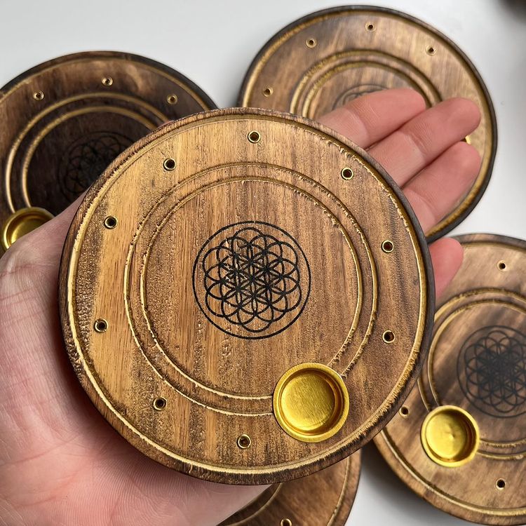 A hand holding a circular wooden incense burner dish to show its portable size, natural grain textures, and multiple stick placement holes.