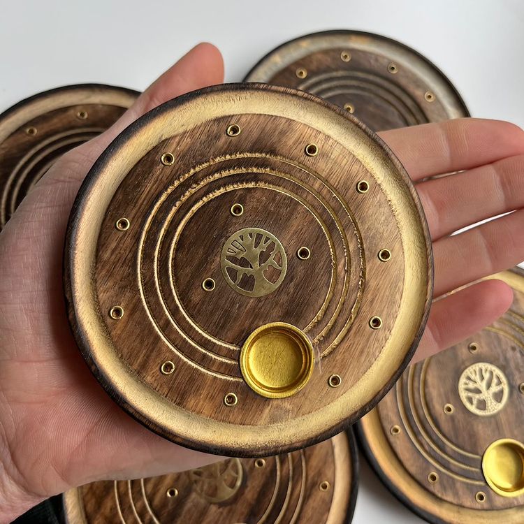 A hand holding a round 10-centimetre mango wood burner plate, displaying its compact size and functional design perfect for burning both incense sticks and fragrance cones during cosy home meditation rituals.