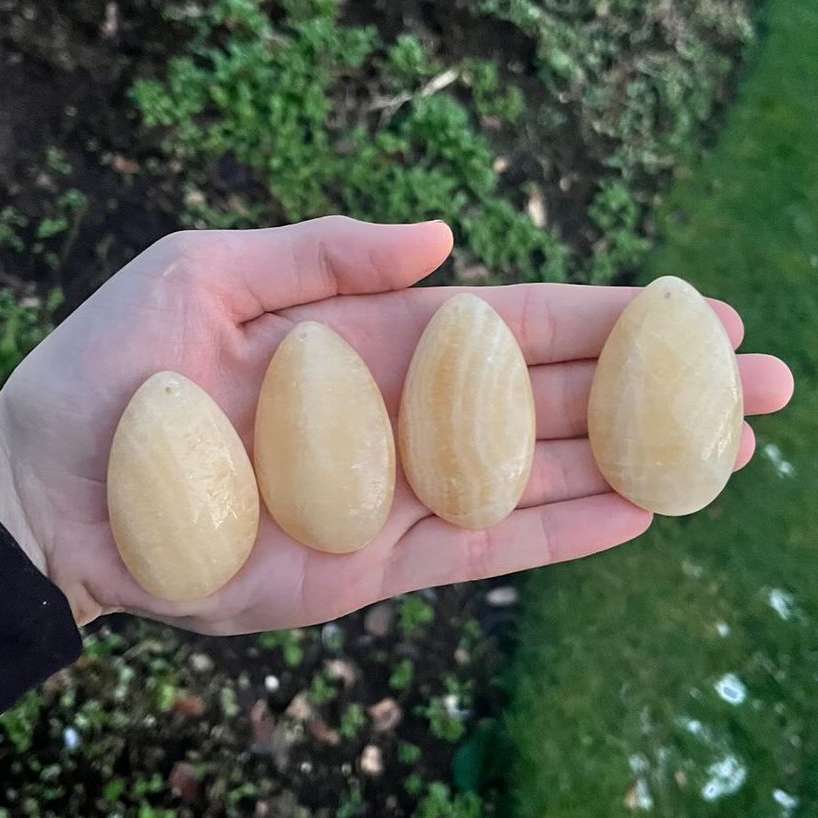 A close-up view of four smooth, polished yellow calcite teardrop crystals resting flat across an open palm outdoors